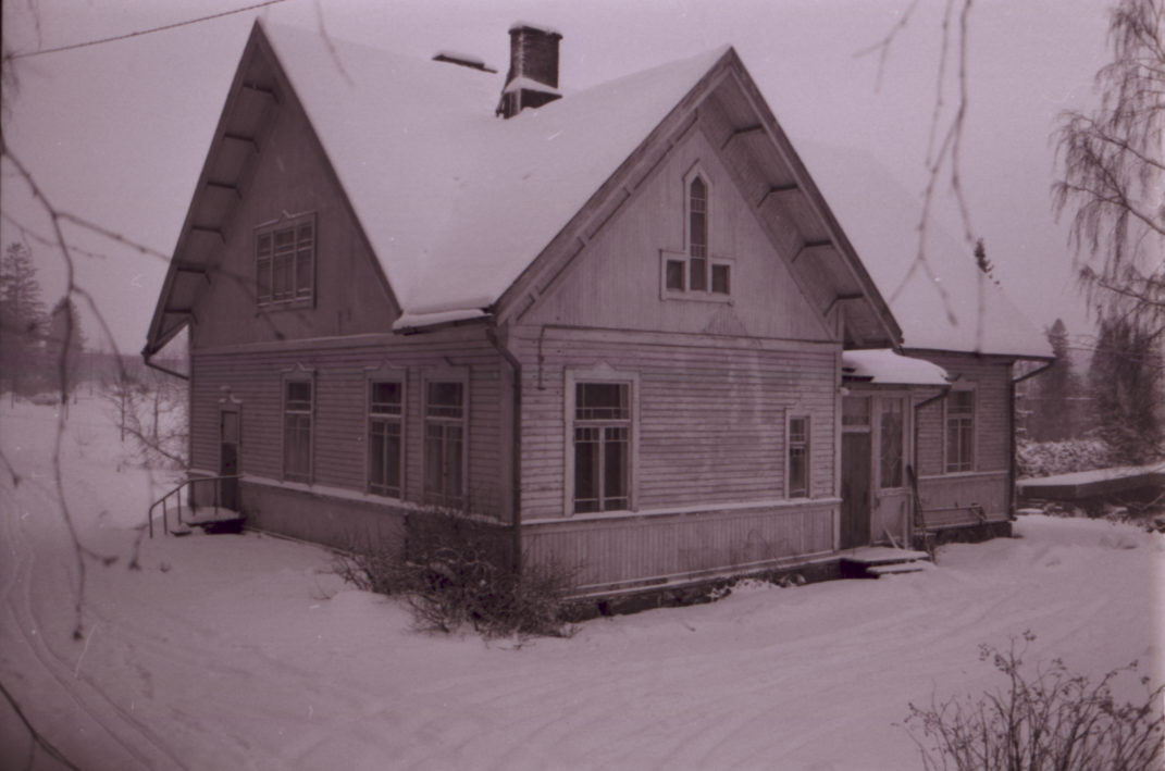 Valkoinen jyrkkäkattoinen rakennus talvisessa maisemassa.