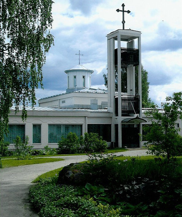 Valkoinen matala kirkkorakennus jonka edessä korkea kellotorni.