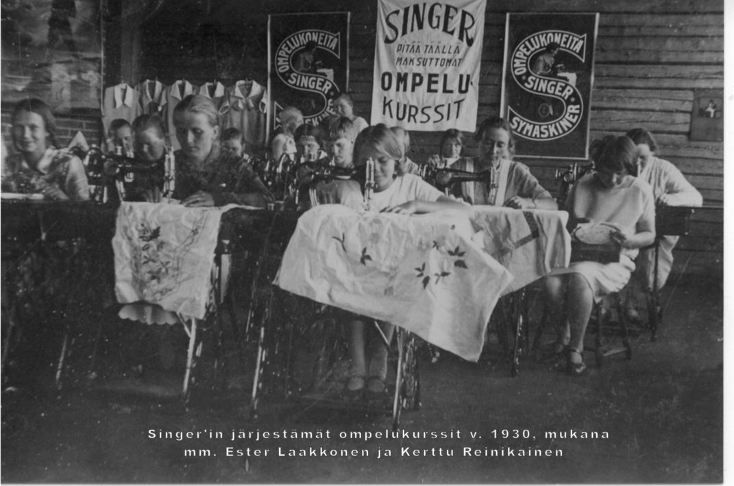 Noin viisitoista ihmistä etualan ihmiset ompelevat ompelukoneilla kuvassa teksti Singerin järjestämät ompelukurssit v. 1930 mukana mm Ester Laakkonen ja Kerttu Reinikainen.